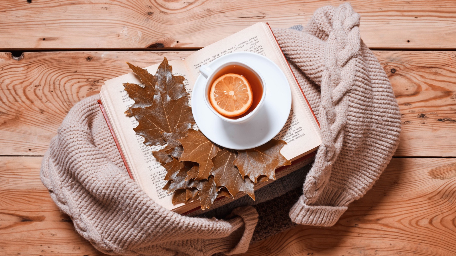 Чашка чая с лимоном на столе с книгой и теплой кофтой