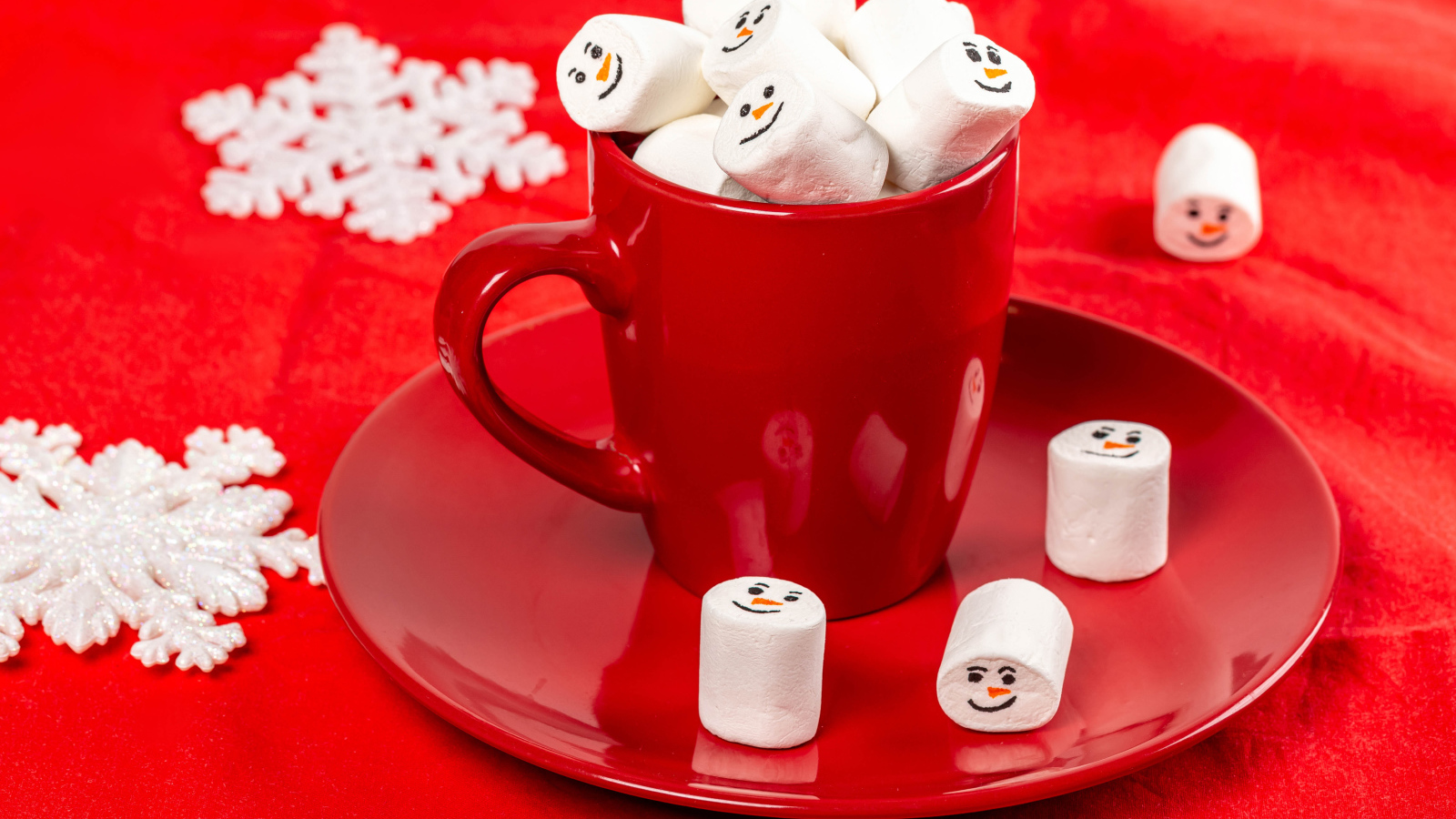 Красная чашка с маршмеллоу на столе со снежинками