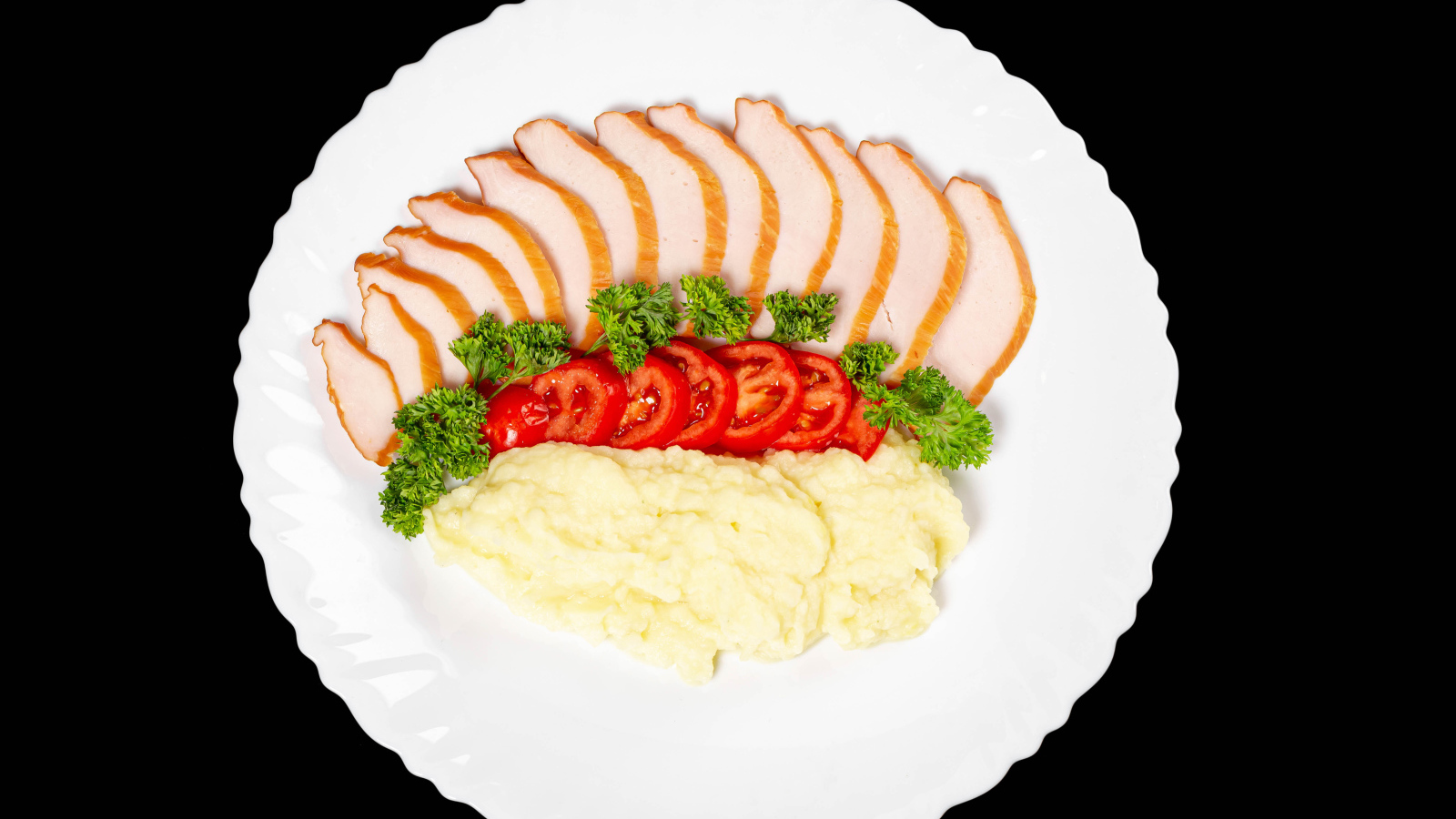 Ham on a large white plate with potatoes and tomatoes