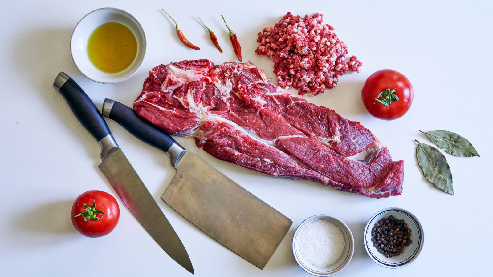 Кусок мяса со специями и ножами на столе 