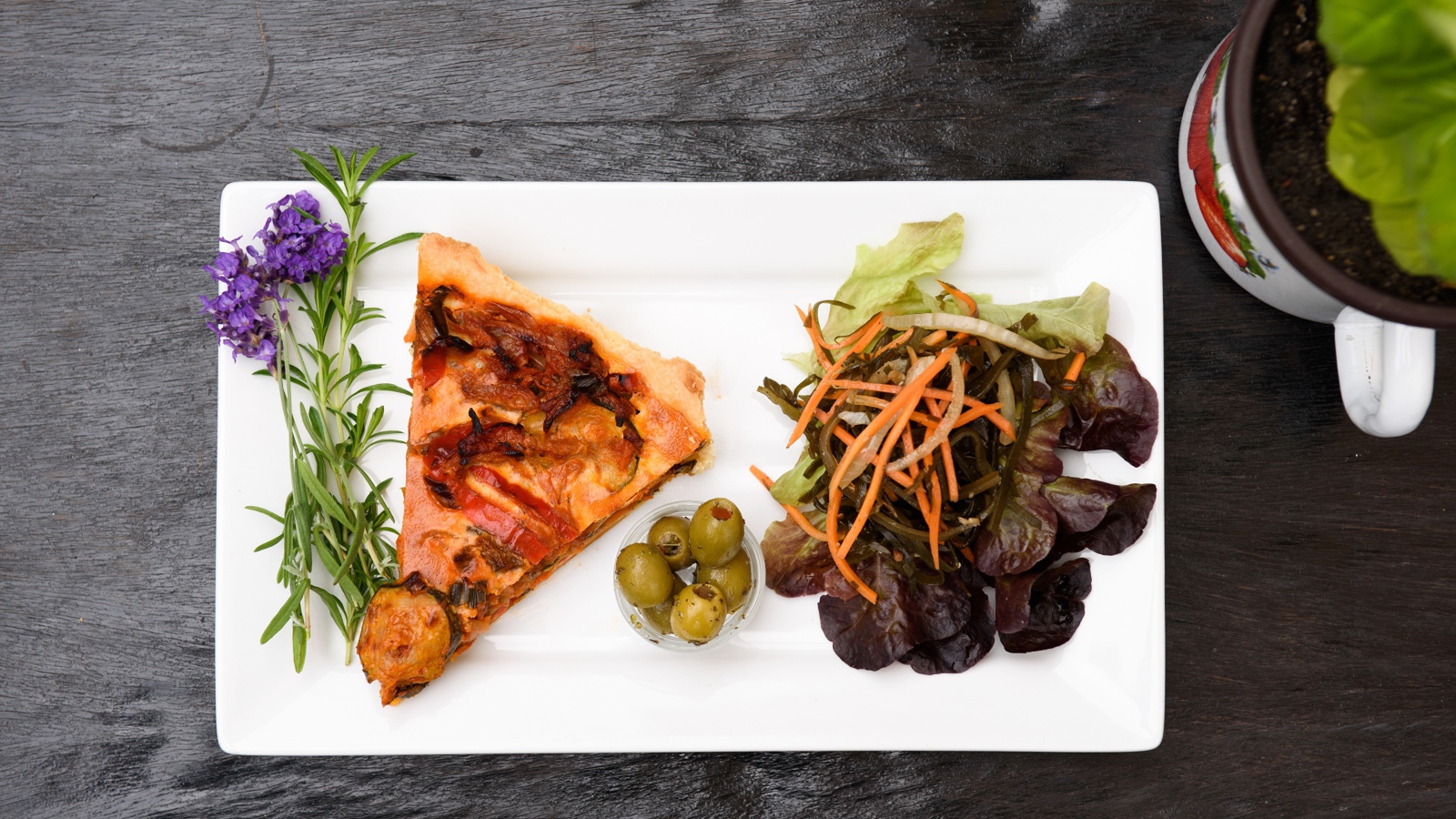 Кусок пиццы с салатом и оливками на белой тарелке