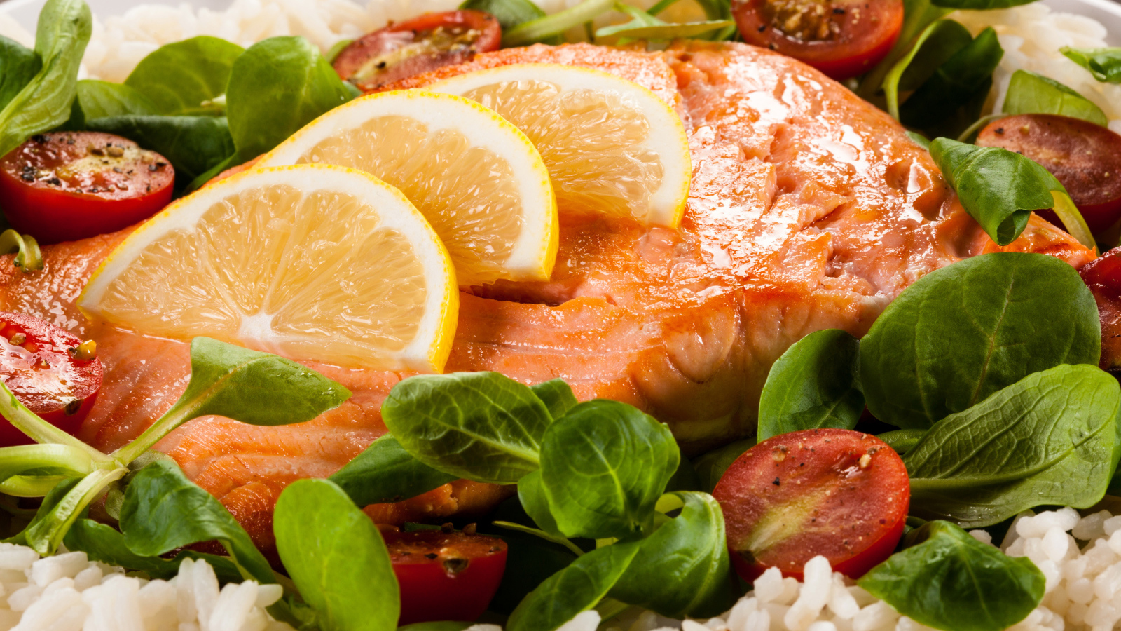 Кусок запеченной красной рыбы на тарелке с лимоном, рисом, базиликом и помидорами