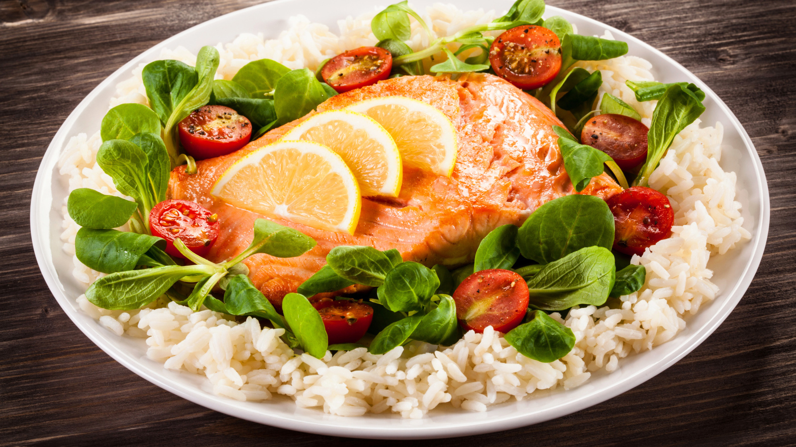 Кусок рыбы на тарелке с помидорами, рисом и листьями базилика 