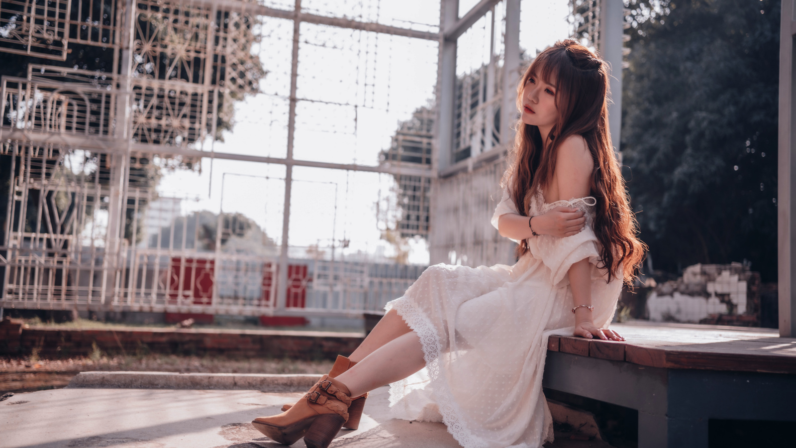 Красивая девушка азиатка в белом платье сидит на лавочке