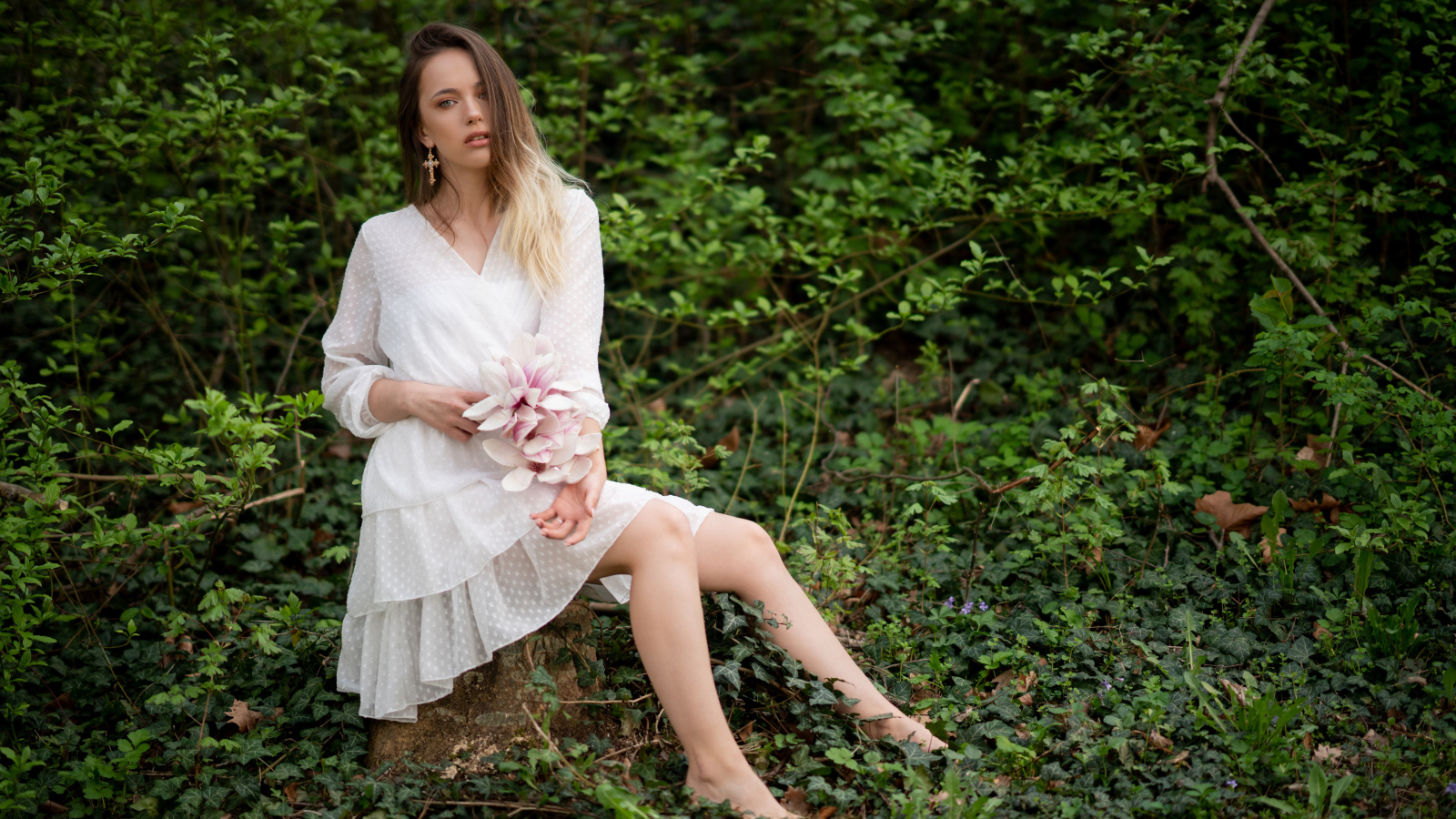 Молодая девушка в белом платье сидит на камне в лесу 