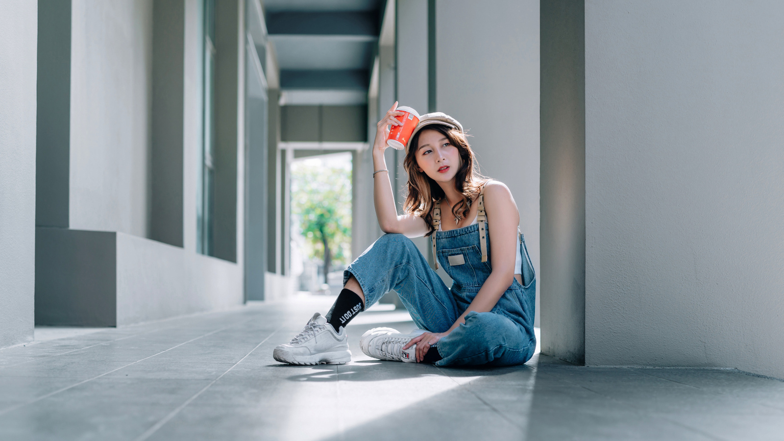 Девушка азиатка в синем комбинезоне с кофе в руке 