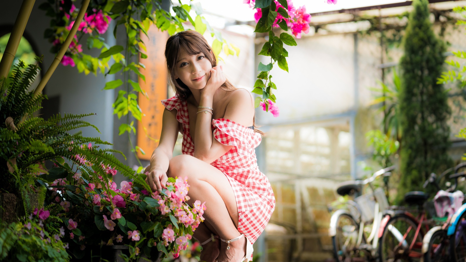 Девушка азиатка сидит на корточках у розового цветка