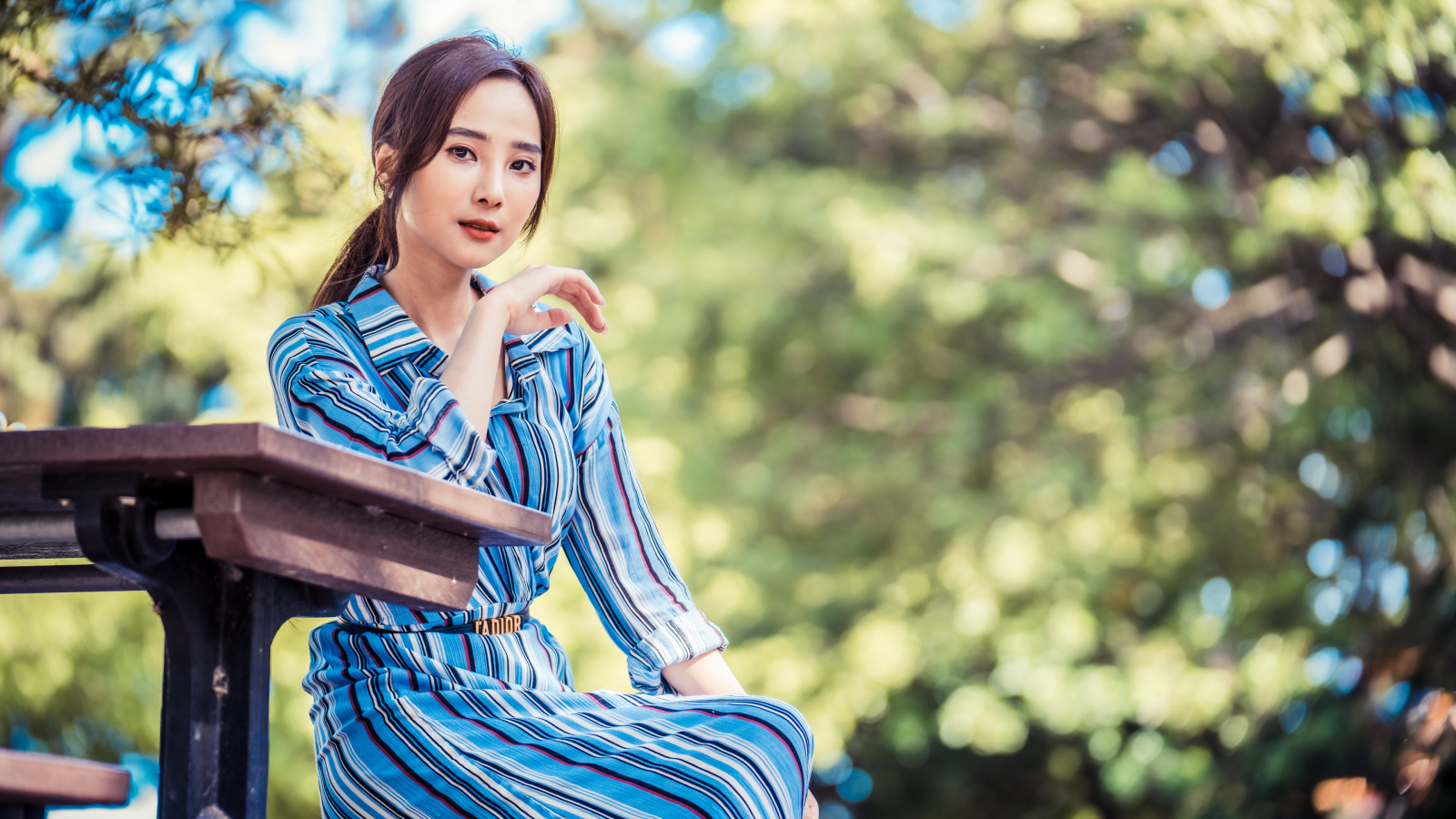 Красивая девушка азиатка в платье  за столом в парке 