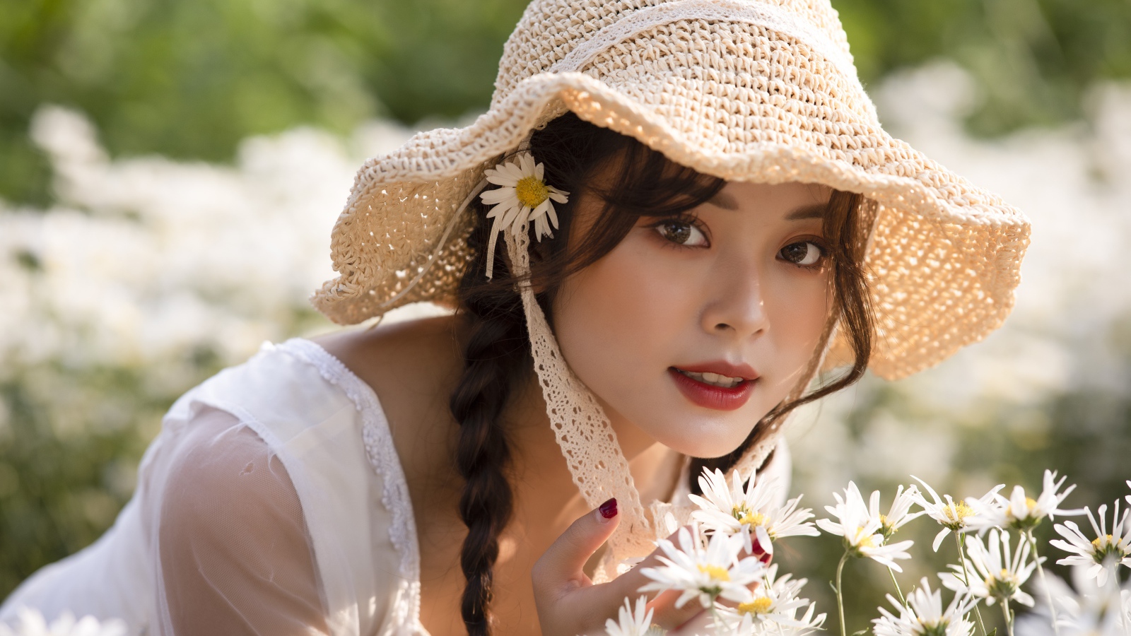Красивая девушка в шляпе на поле с ромашками 