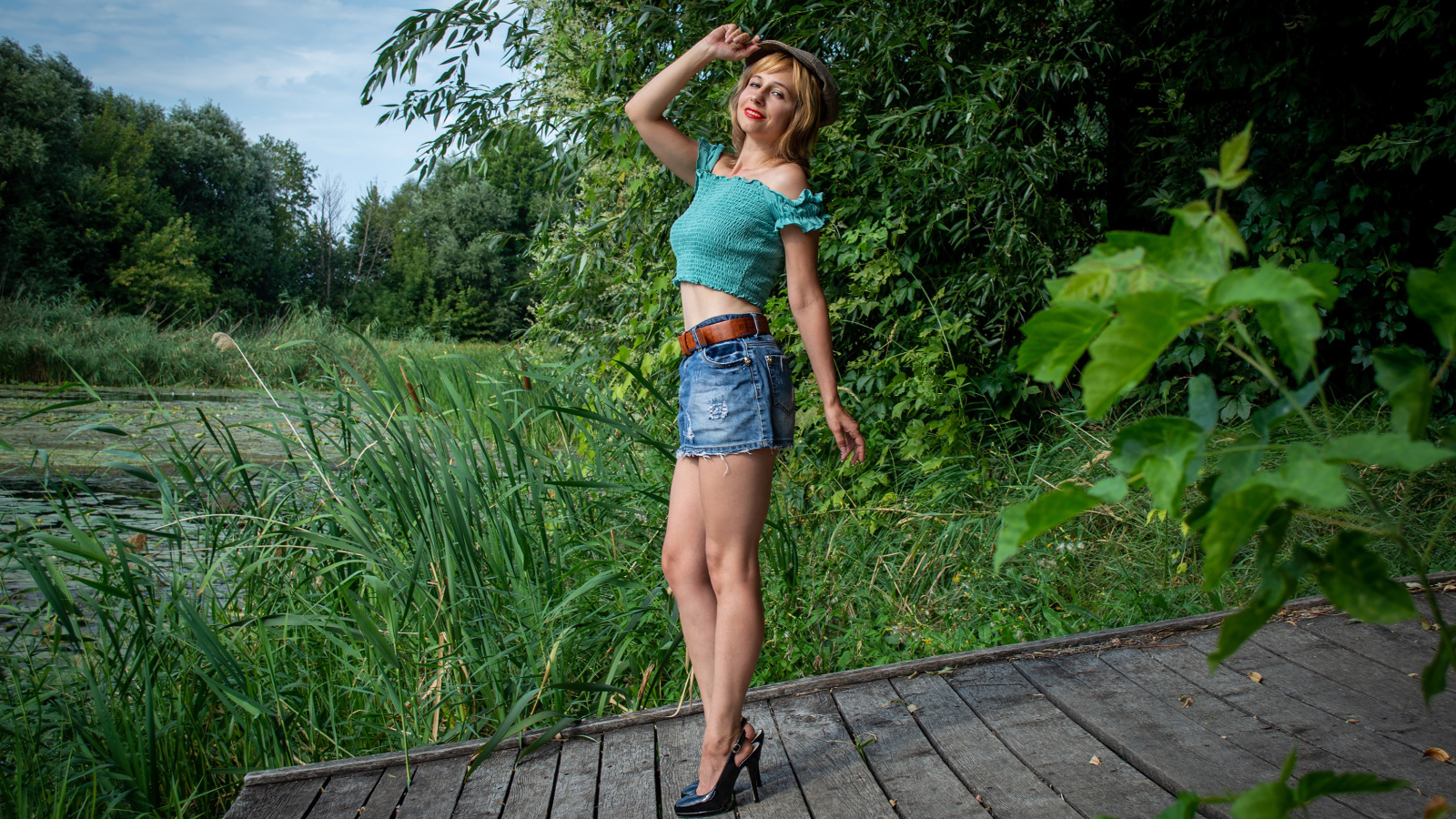 Красивая девушка в джинсовой юбке у пруда 