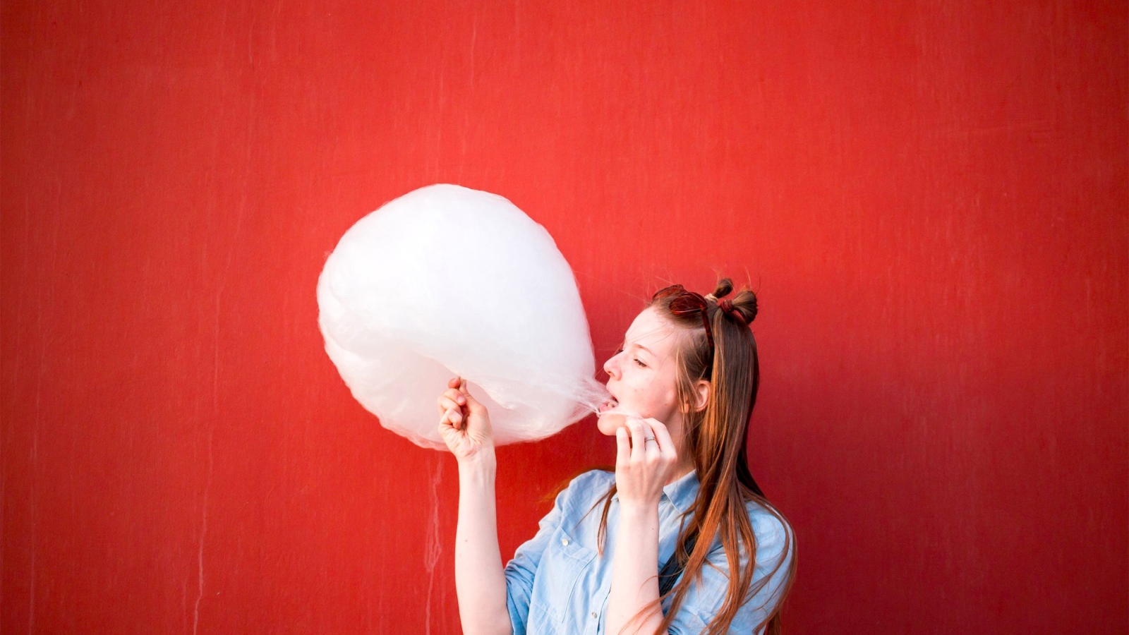 Девушка ест сладкую вату на красном фоне 