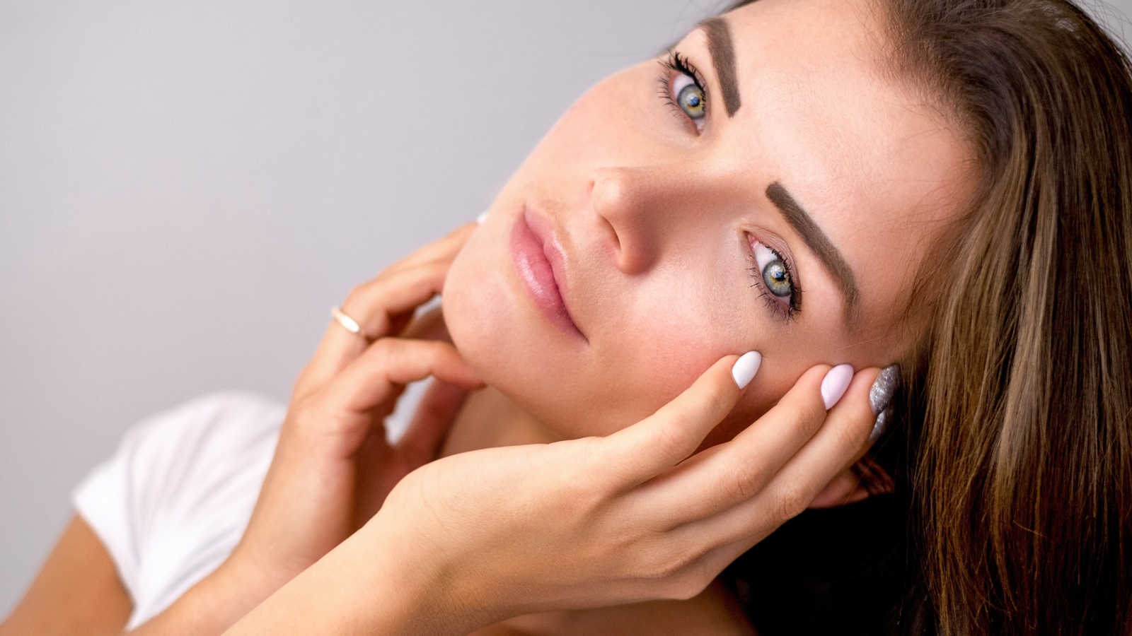 Девушка с руками у лица на сером фоне