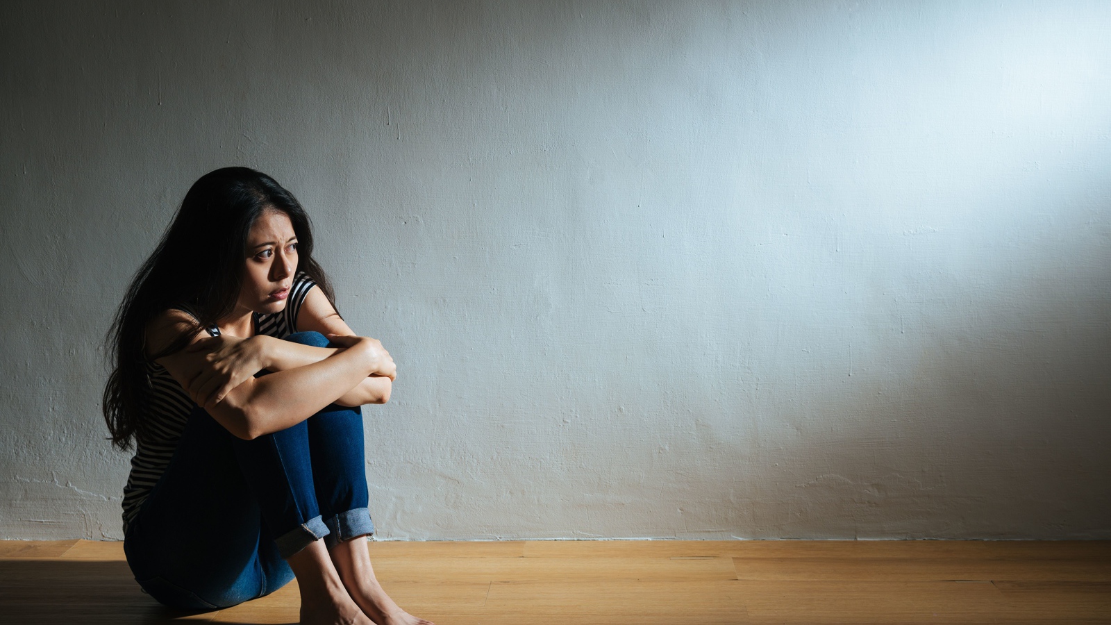 Испуганная девушка азиатка сидит у стены