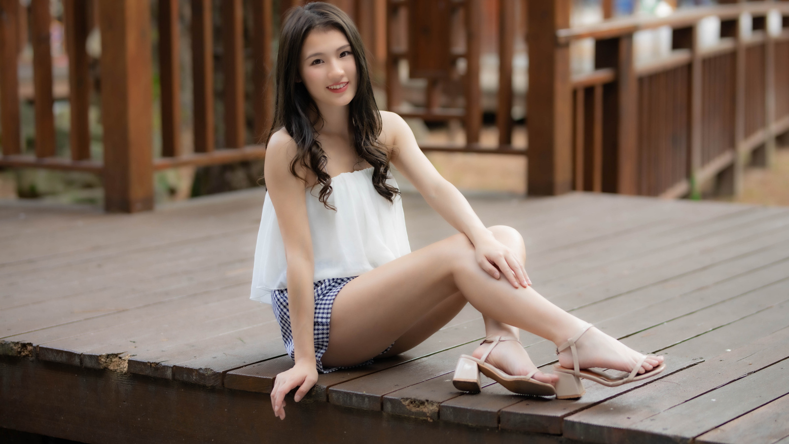 Улыбающаяся девушка азиатка сидит на мосту 