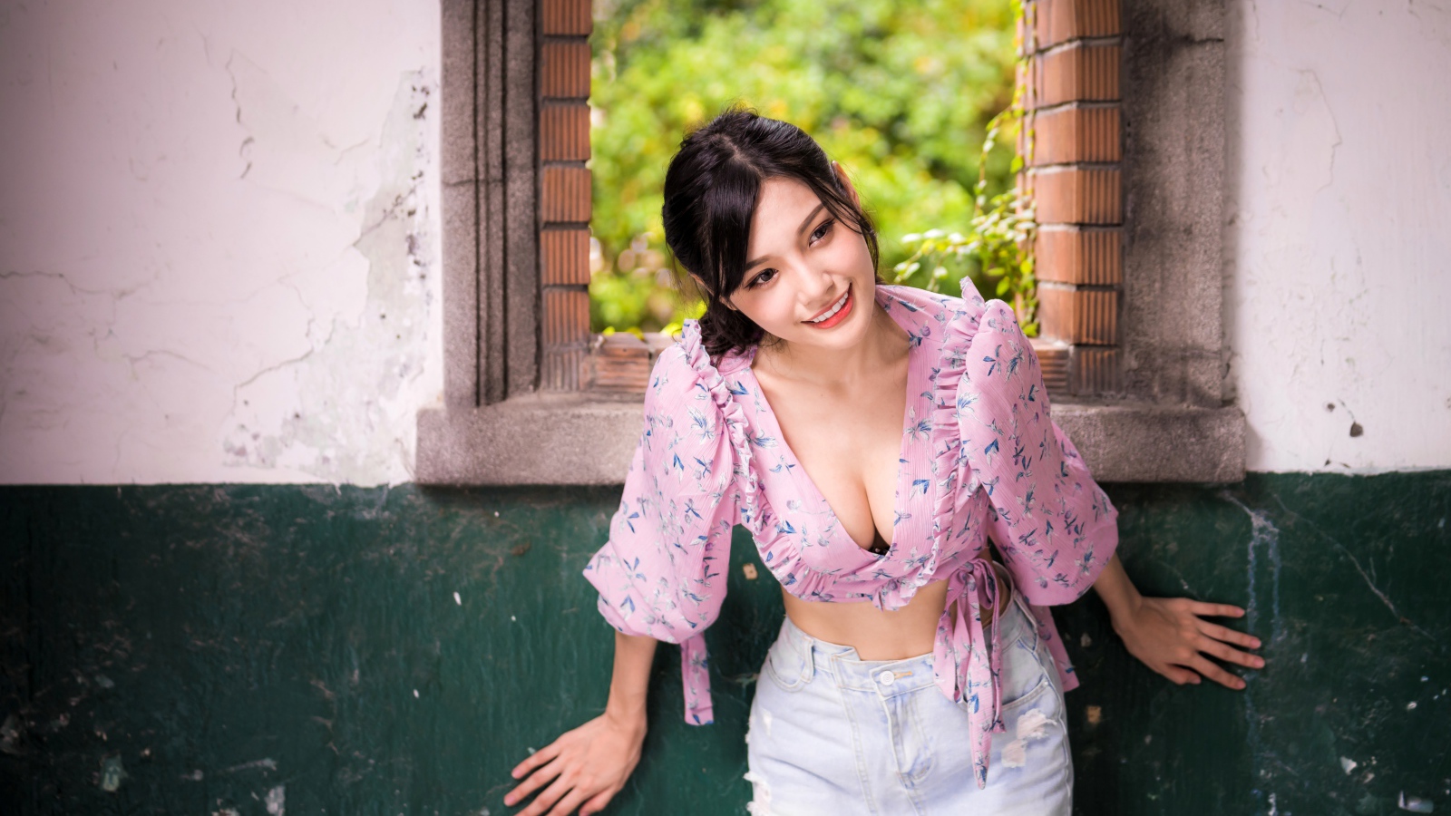 Улыбающаяся девушка азиатка стоит у окна 