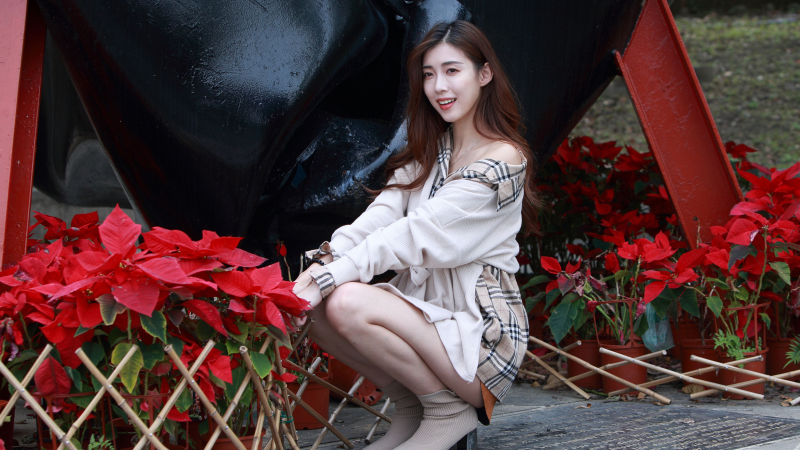 Улыбающаяся азиатка сидит у красных цветов 