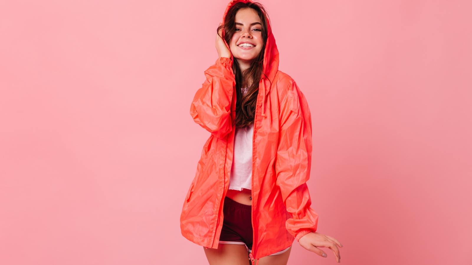 Улыбающаяся девушка в плаще на розовом фоне