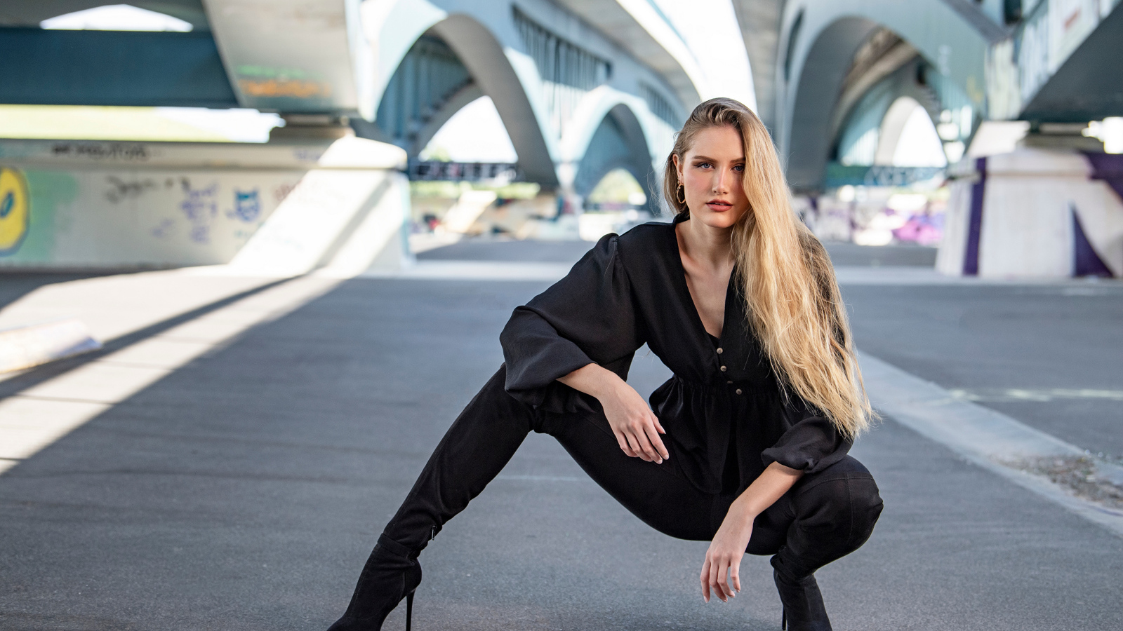 Стильная девушка в черном костюме под мостом