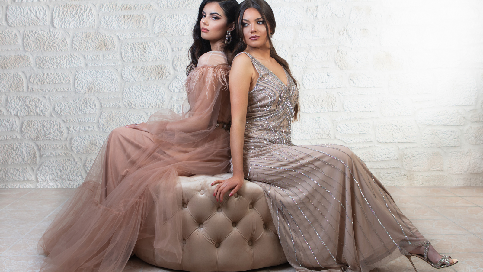 Две девушки в красивых платьях сидят на диване 