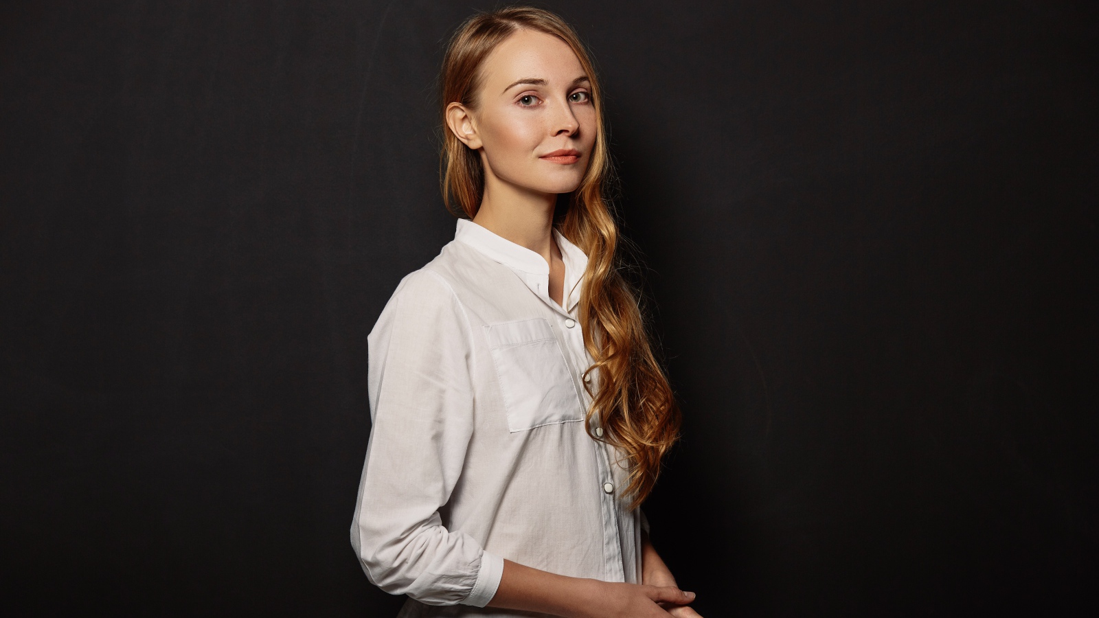 Молодая девушка в белой рубашке на фоне черной стены 