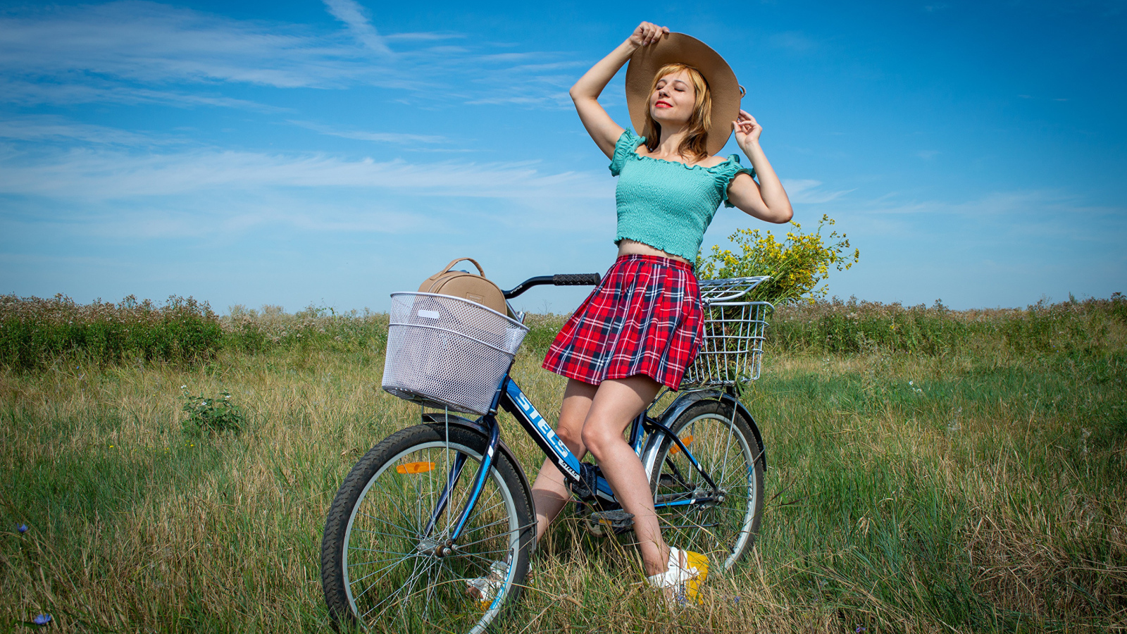 Молодая девушка на велосипеде на поле под голубым небом 