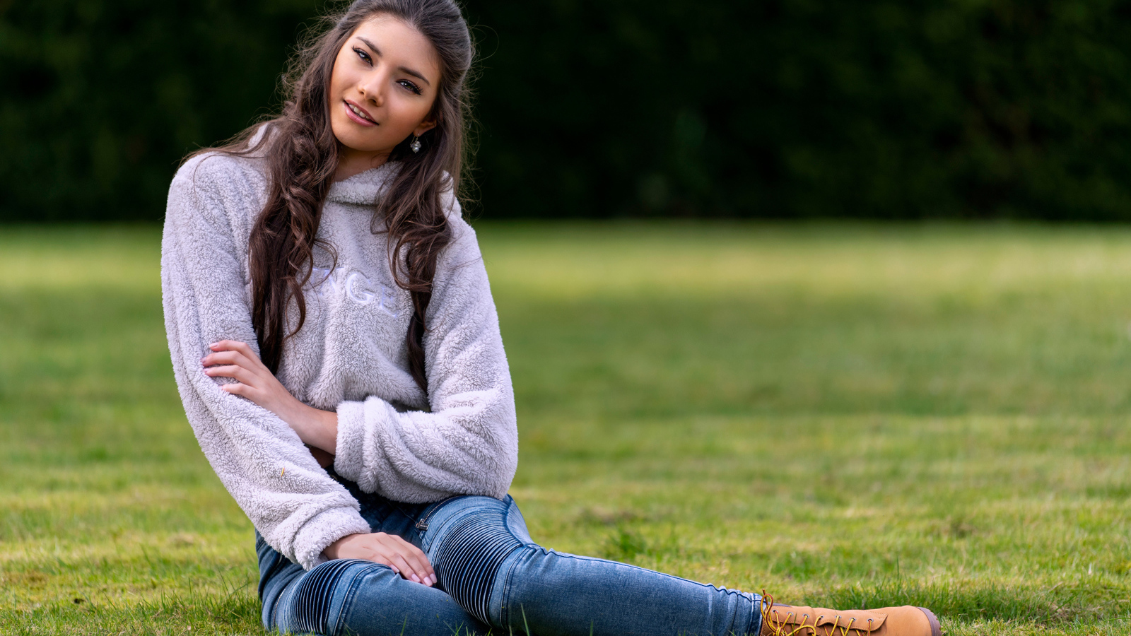 Молодая длинноволосая девушка сидит на траве 