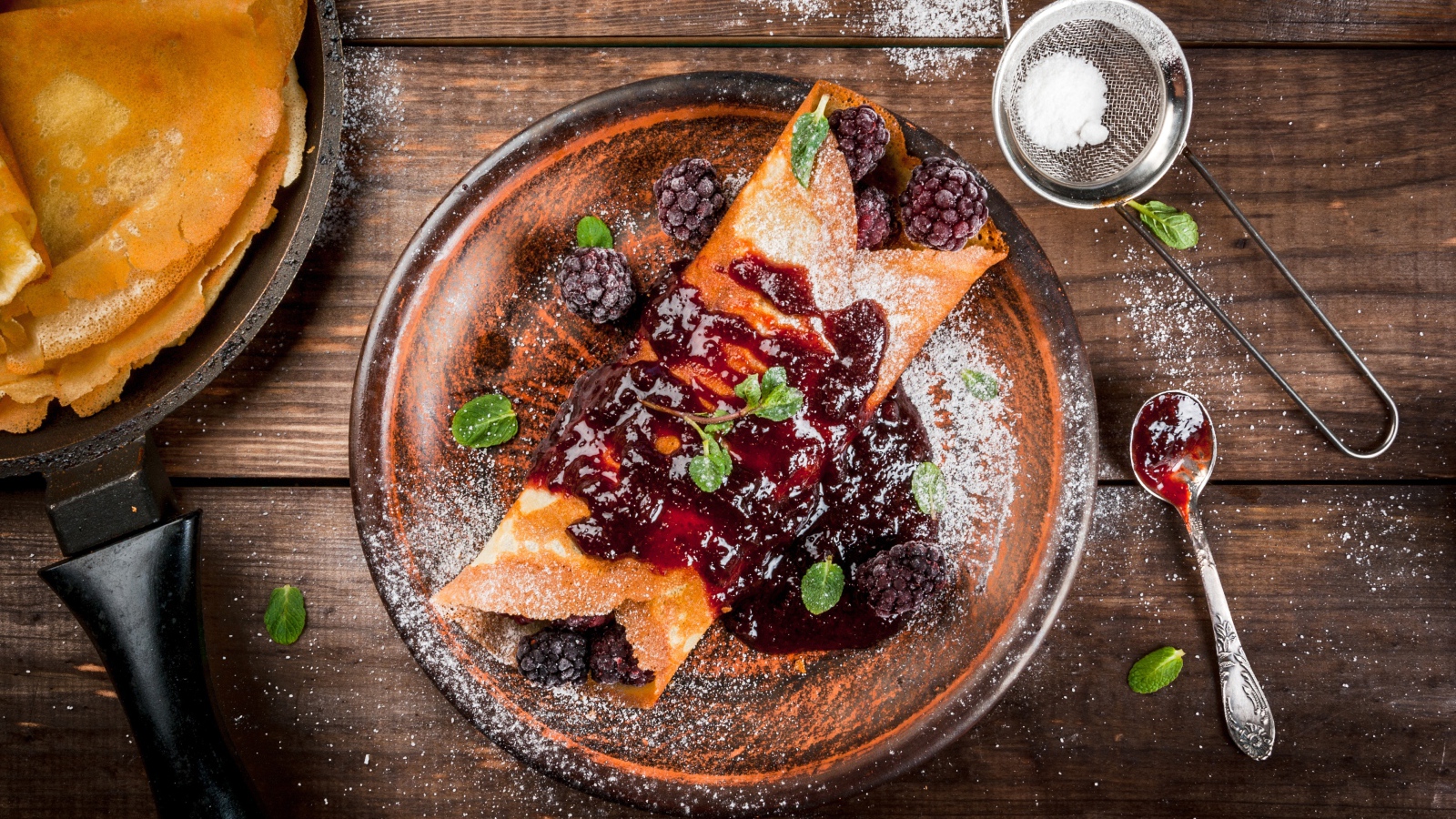 Блин с ягодами и джемом на тарелке с сахарной пудрой