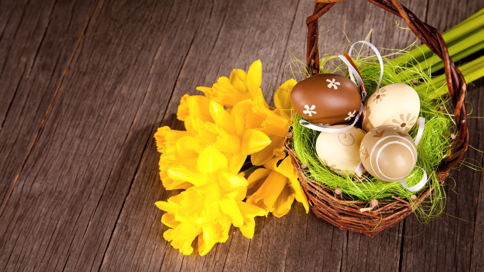 Корзина с крашеными пасхальными яйцами на столе с букетом нарциссов