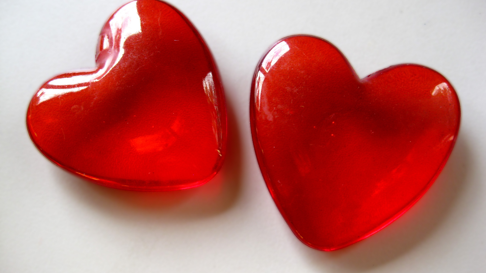 Два красных стеклянных сердца на сером фоне