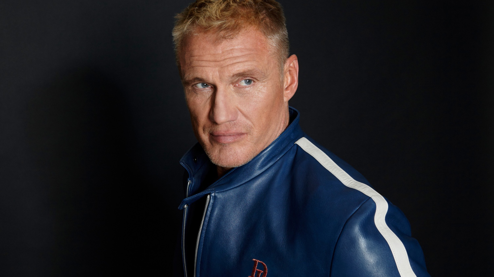 Актер Дольф Лундгрен в куртке на фоне  серой стены