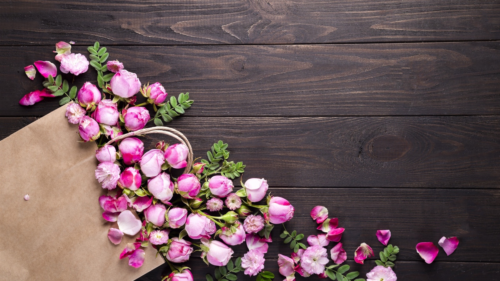 Цветки розовой розы с бумажным пакетом  на деревянном фоне