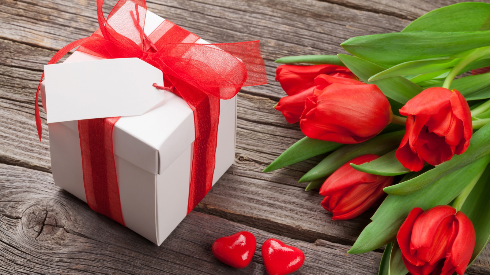 Красные тюльпаны с большим подарком на деревянном столе 