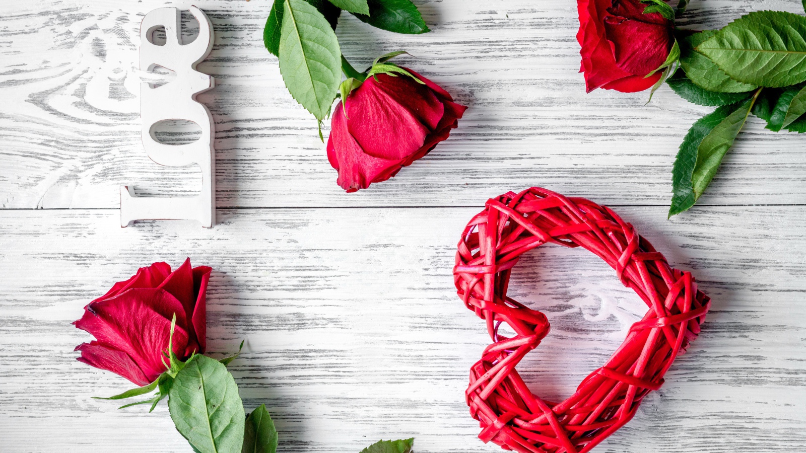 Красное плетеное сердце с алыми розами на деревянном столе