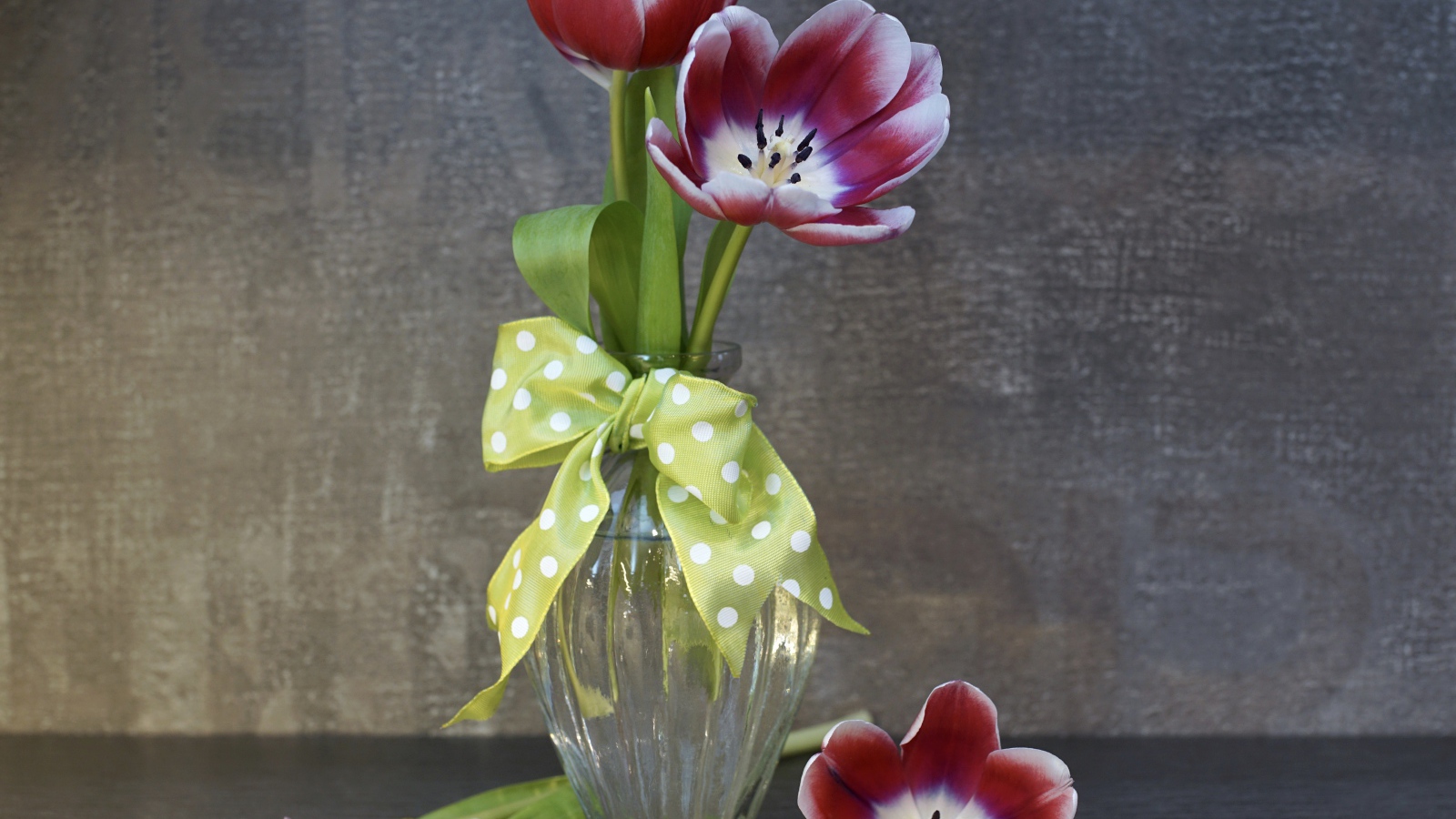 Три розовых цветка тюльпана в стеклянной вазе у стены