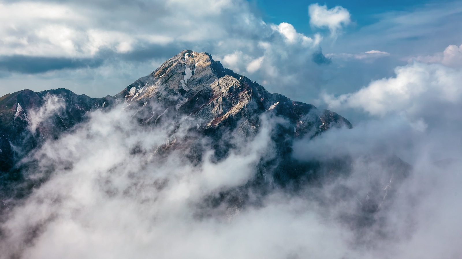 Большая высокая гора в густых белых облаках