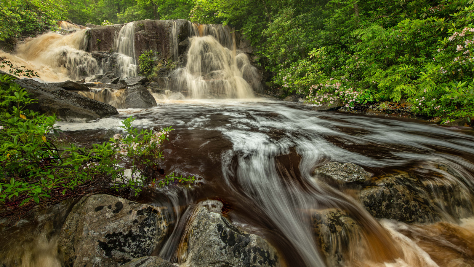 Быстрая холодная вода водопада стекает по большим камням