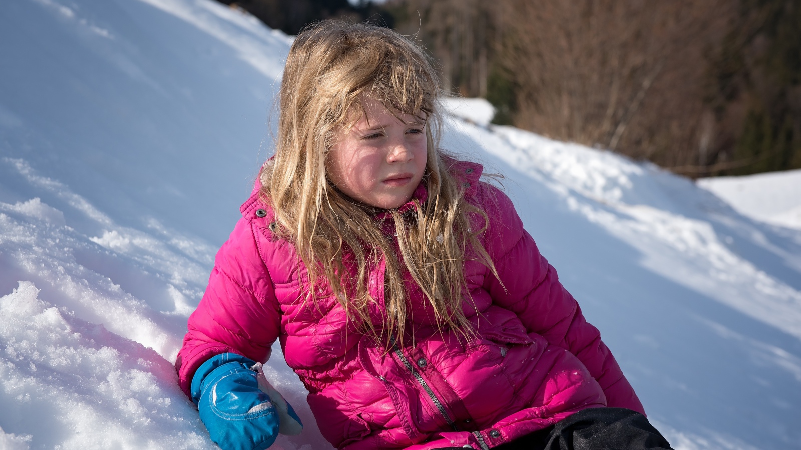 Маленькая девочка лежит на заснеженной горке 