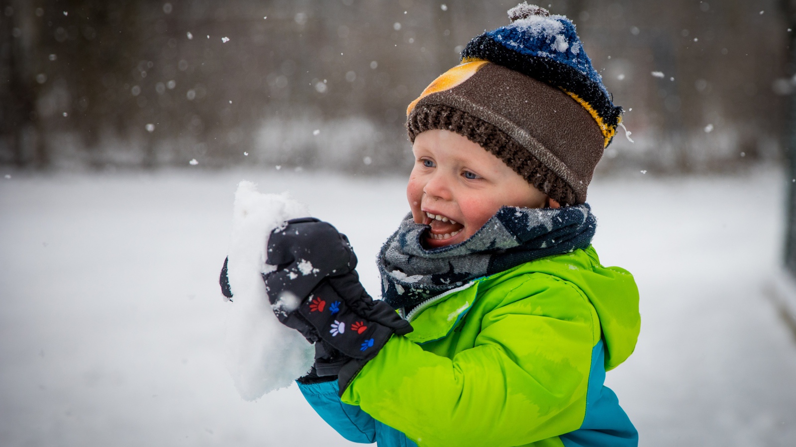 Веселый маленький мальчик со снегом в руках 