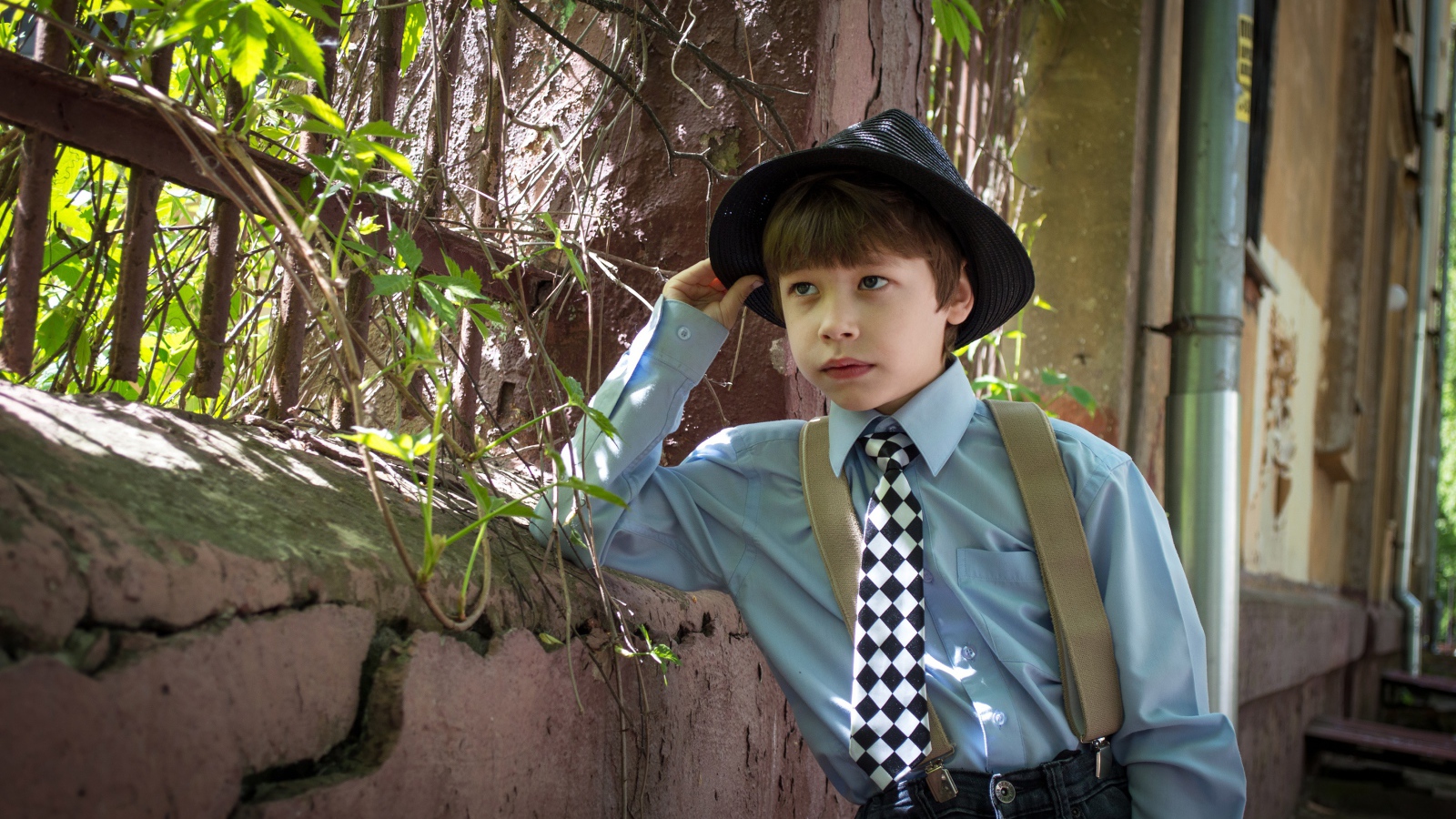 Красивый мальчик в шляпе стоит у забора 