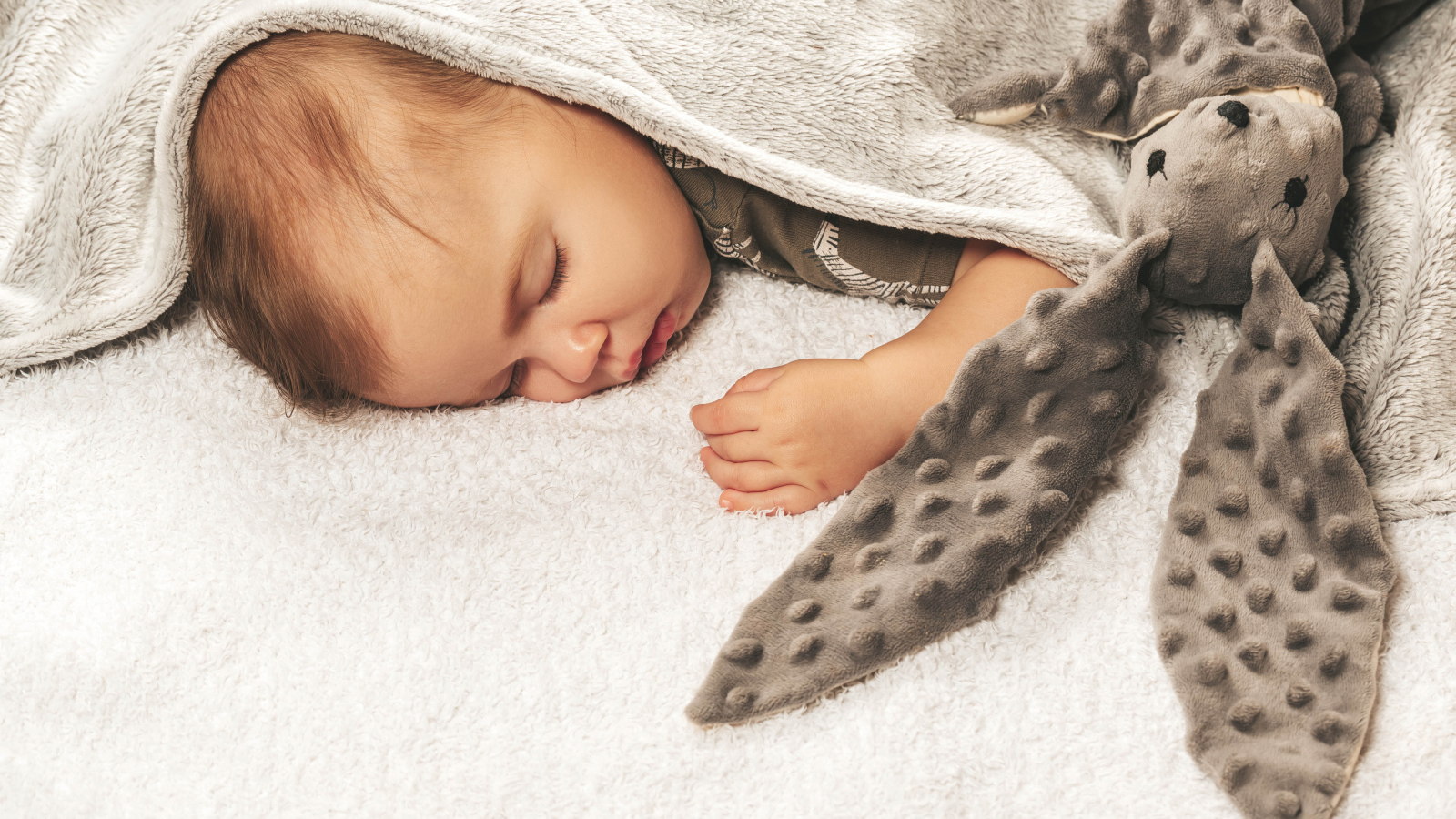 Маленький ребенок спит с игрушкой под одеялом