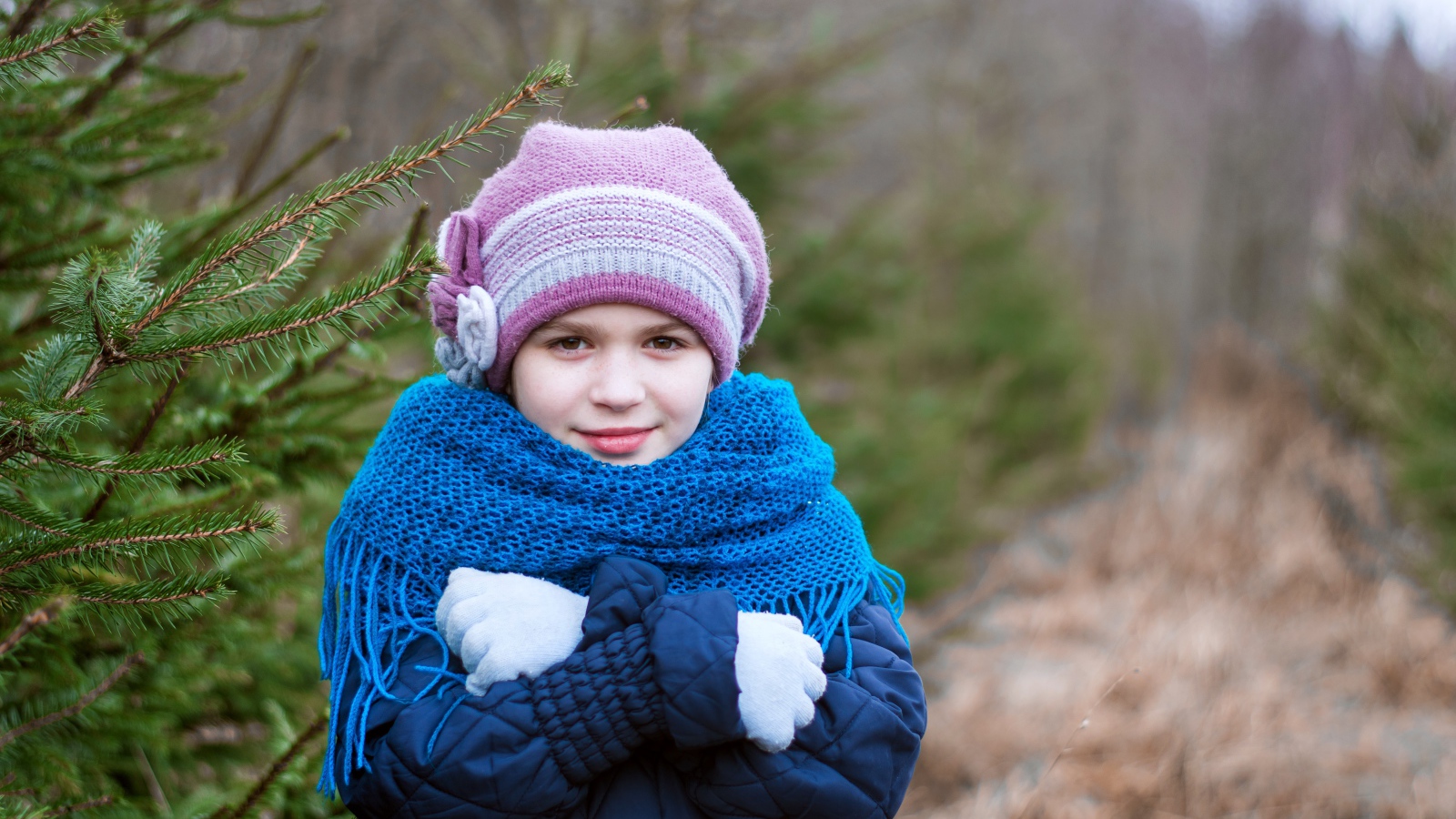 Маленькая девочка в теплой одежде у ели