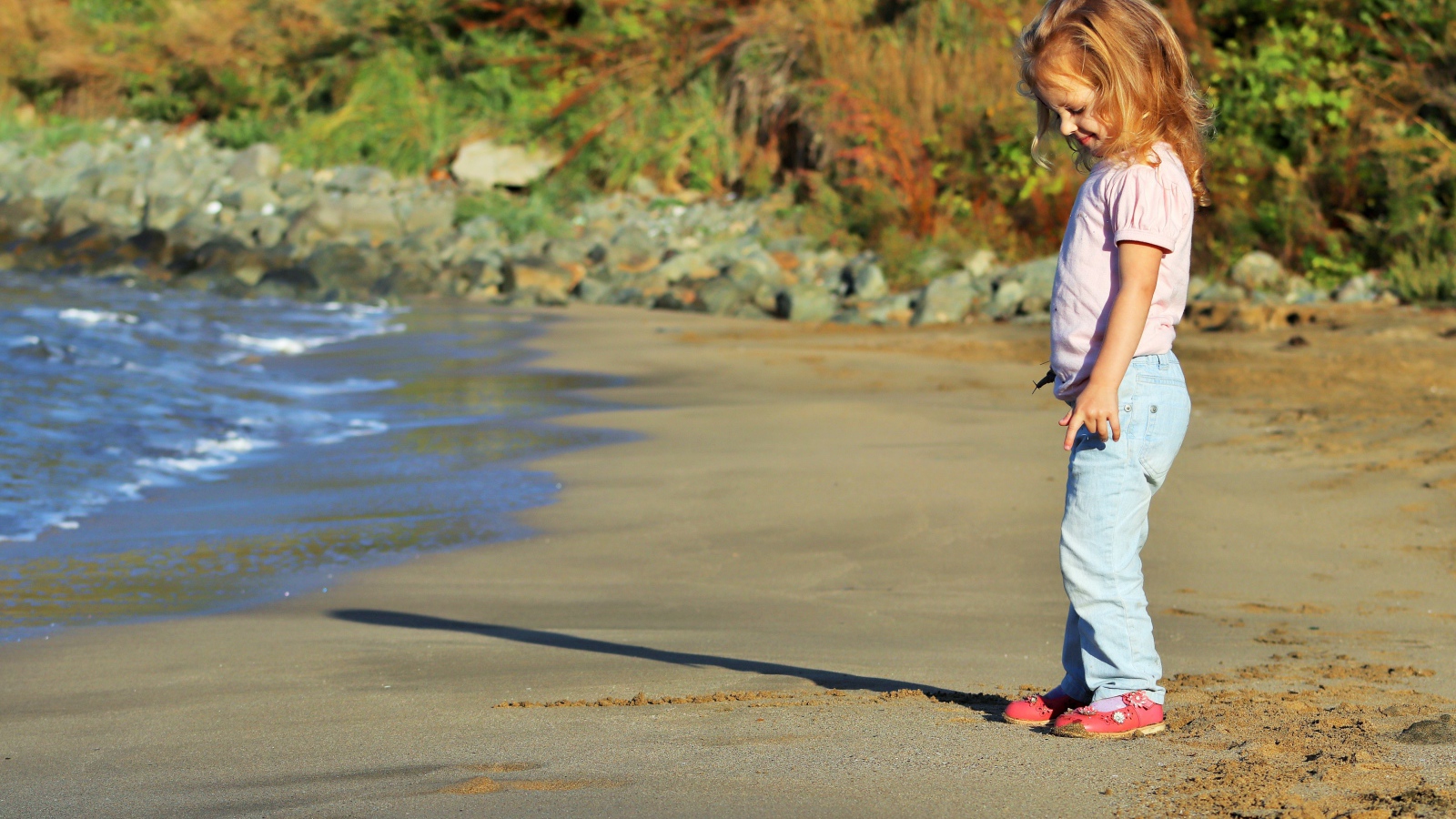Маленькая девочка гуляет по мокрому песку 