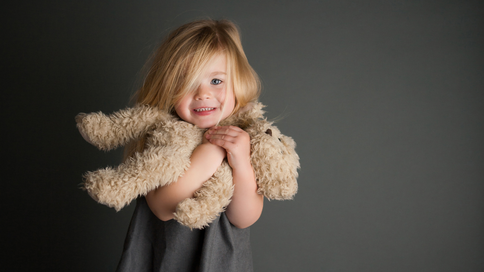 Маленькая девочка с игрушечным медвежонком в руках  на сером фоне 