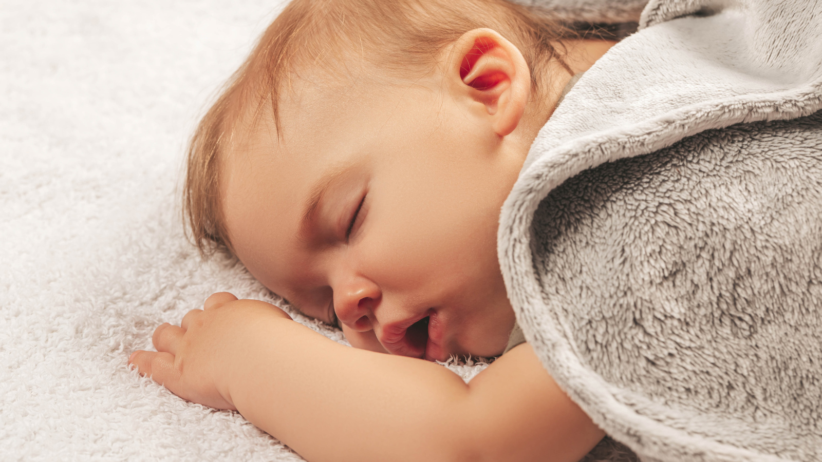 Маленький спящий ребенок под серым покрывалом 