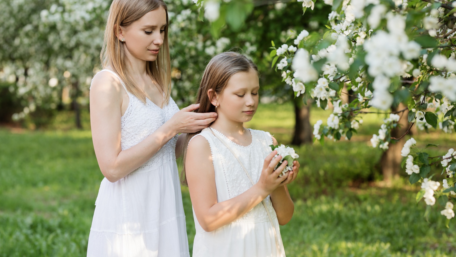 Мама заплетает дочке волосы у дерева