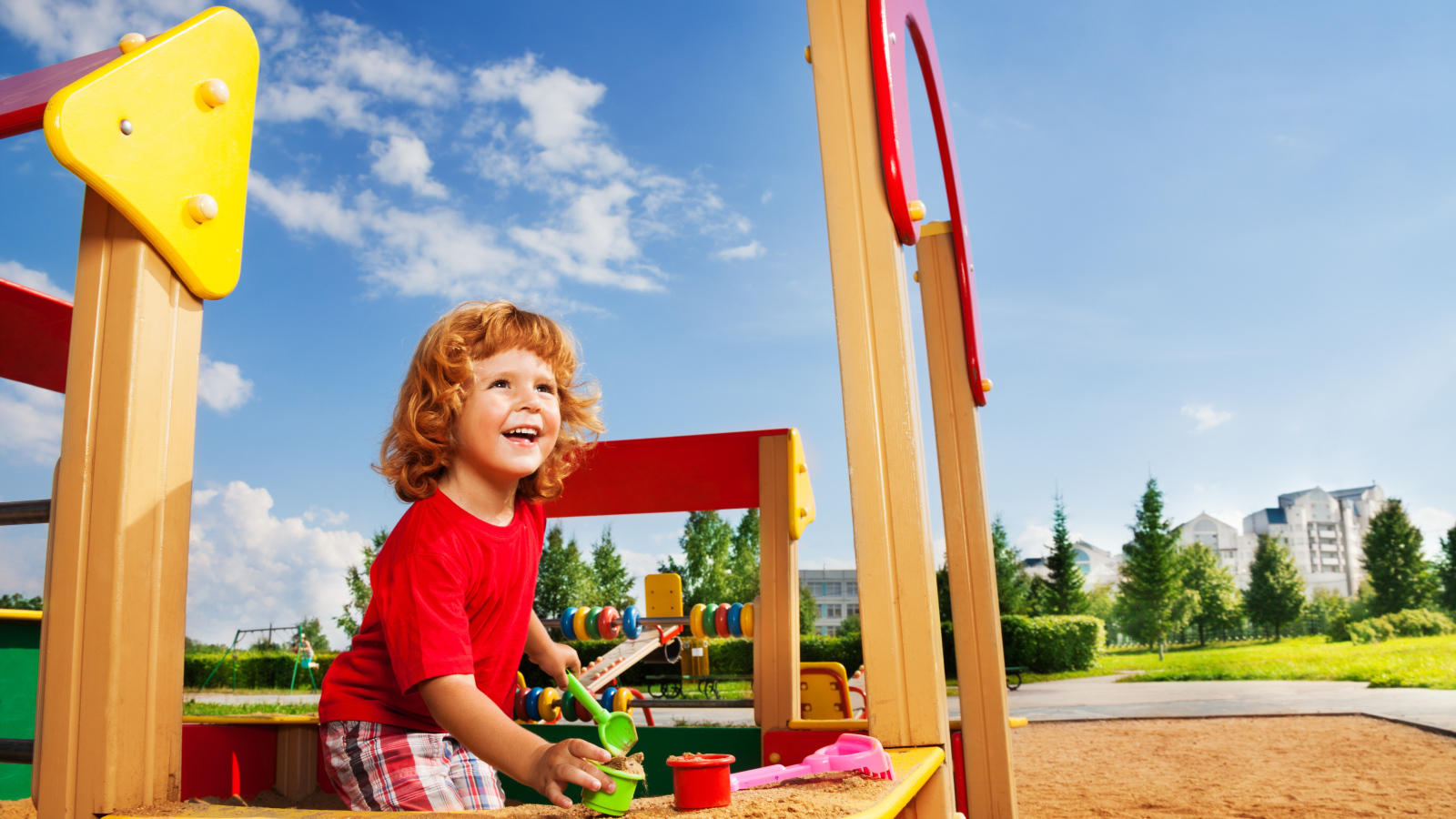 Улыбающийся мальчик в песочнице на детской площадке 