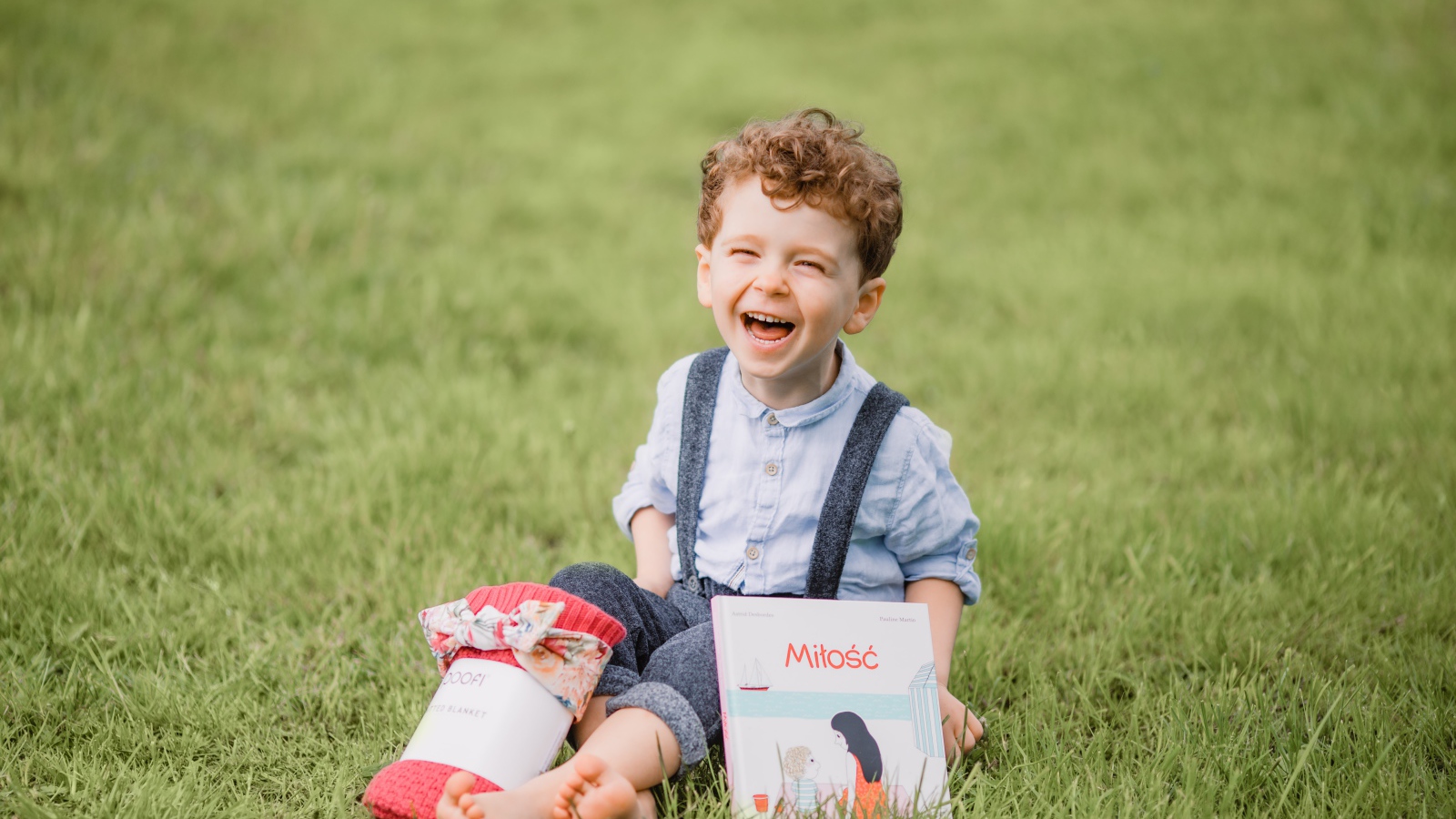 Улыбающийся маленький мальчик сидит на зеленой траве