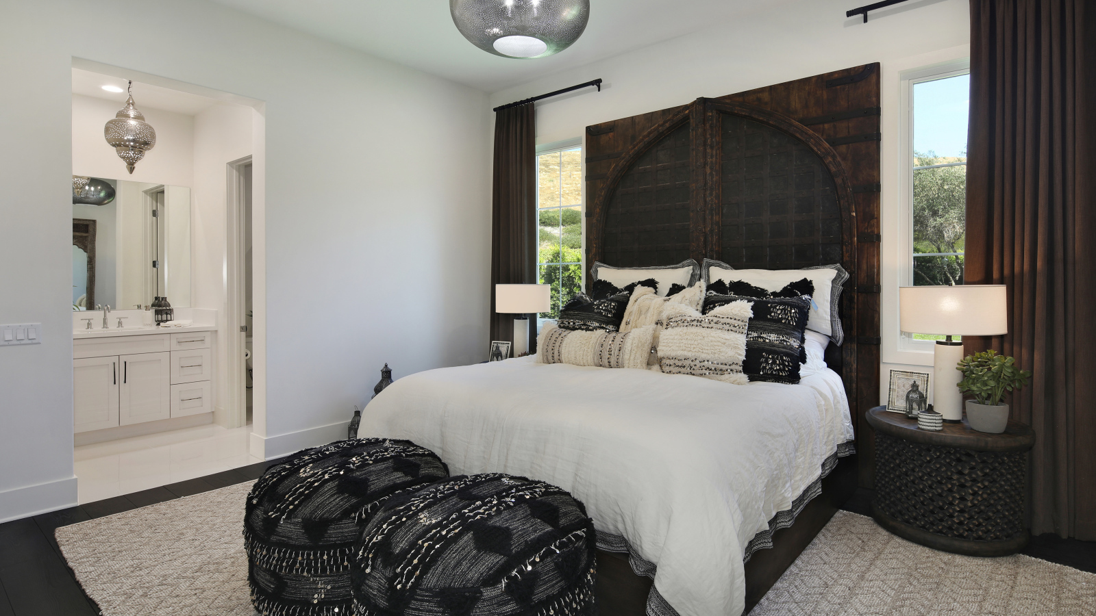 Большая кровать в спальне с большими окнами со шторами