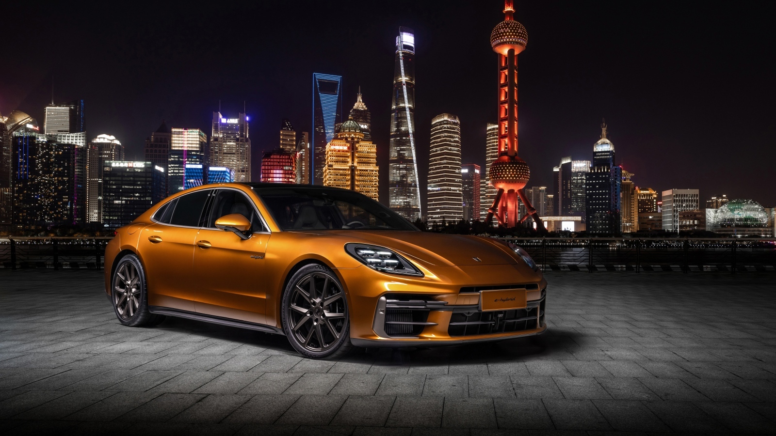 Золотистый автомобиль Porsche Panamera Turbo E-Hybrid 2024 года на фоне города