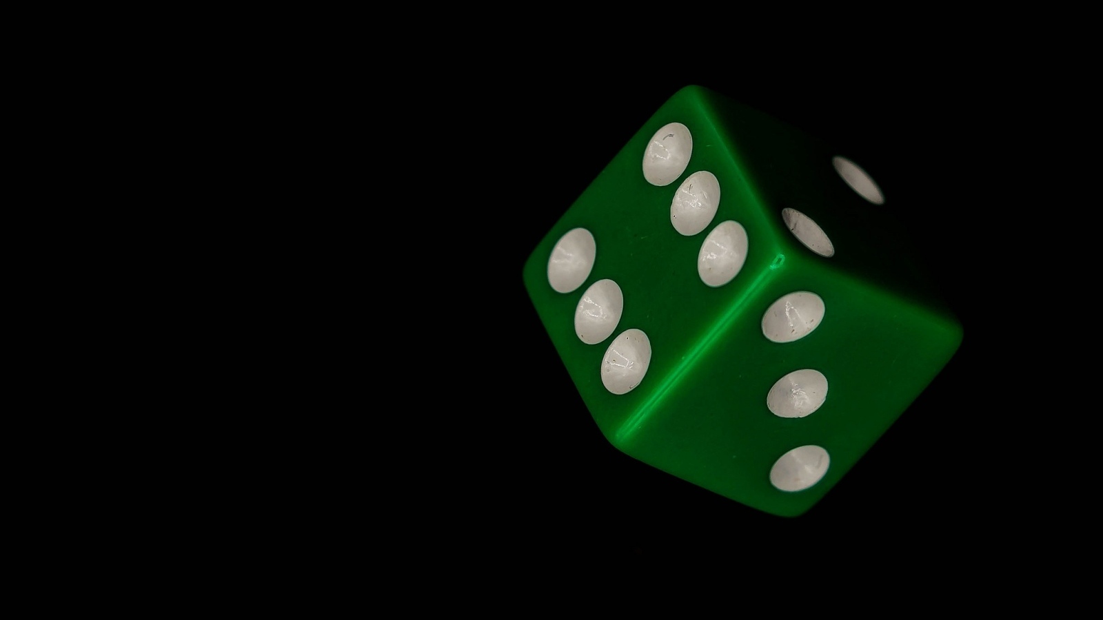 Зеленый игральный кубик на черном фоне